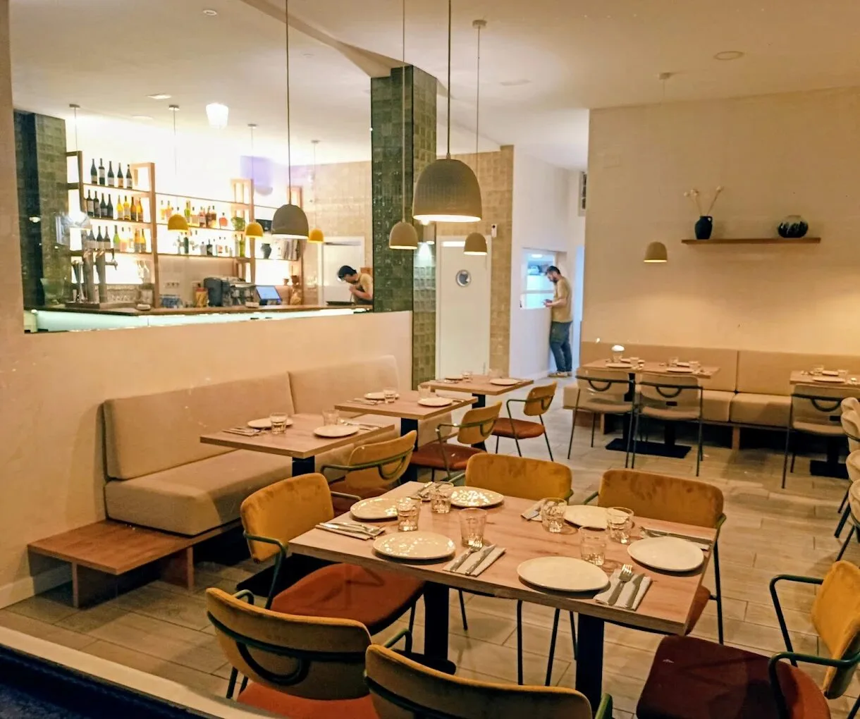 Sala luminosa de Silvestre con mesas vestidas, sillas de colores y la barra al fondo.